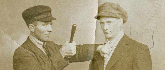 A man in uniform brandishes a club against a man in a suit